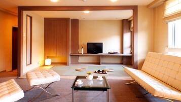 Un salon moderne avec un canapé, un pouf, une table basse en verre et un téléviseur à écran plat.