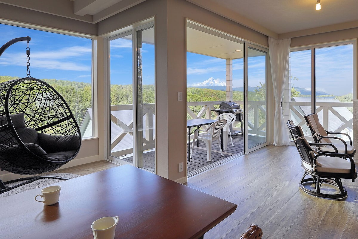 A spacious room with a large sliding glass door leading to an outdoor deck, a hanging chair, a table with two cups, and a fireplace.