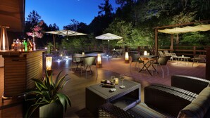 An outdoor patio area with wicker furniture, tables, and chairs, and a bar area with bottles and a candle. - Hotel Ryu Resort and Spa (Takayama)
