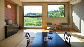 A modern room with tatami mats, a dining table, chairs, and large windows offering a view of a green landscape.