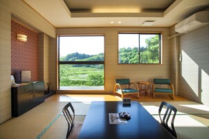 Una habitación moderna con esteras de tatami, una mesa de comedor, sillas y ventanas amplias que ofrecen vistas a un paisaje verde.