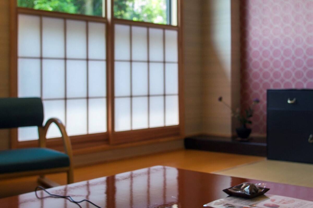 Une pièce avec une table en bois, une chaise verte, un buffet sombre et une fenêtre à carreaux.