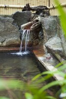 Una pequeña cascada en un entorno natural con rocas y una valla de bambú al fondo.