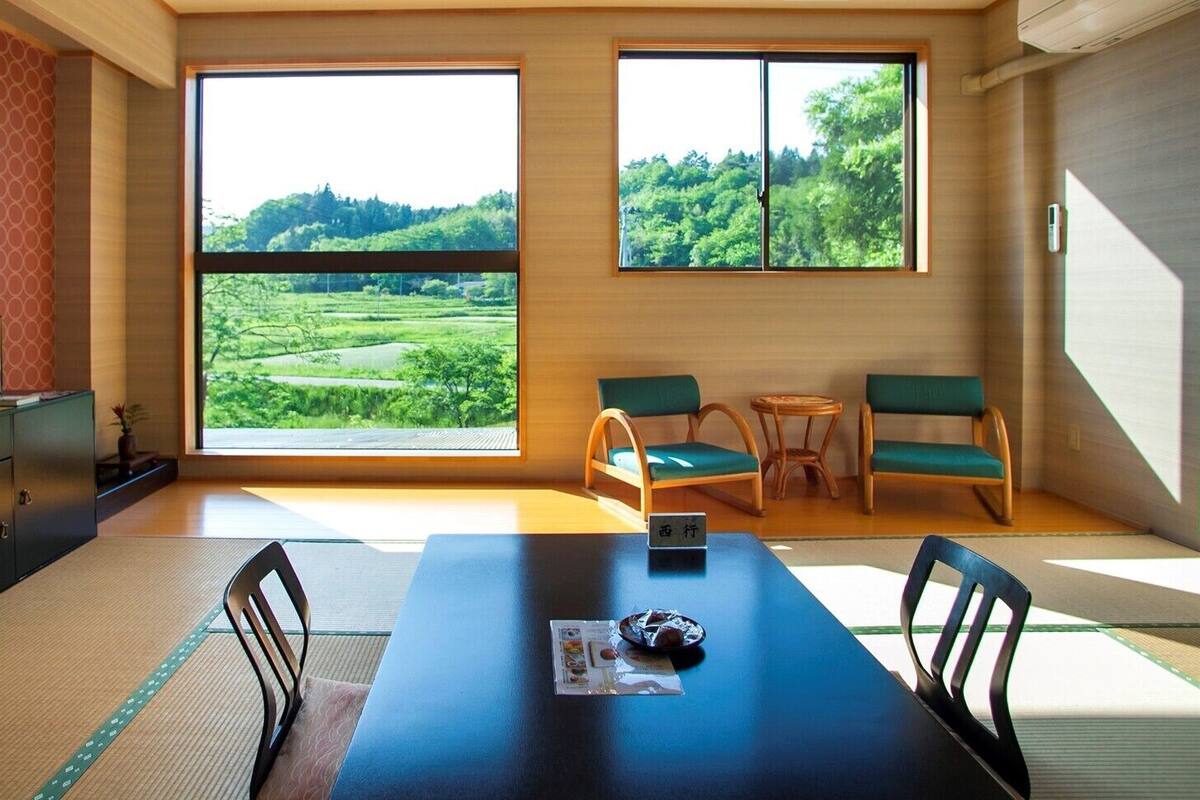Une pièce avec une grande fenêtre, une table à manger, des chaises, un petit meuble et un tatami.