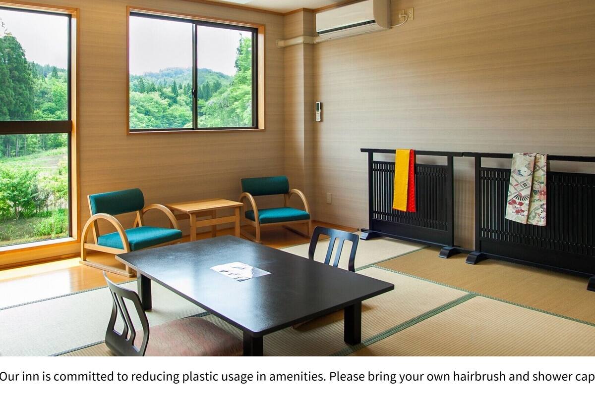 Une pièce avec des tatamis, une table basse, deux chaises et une vue sur la verdure à l’extérieur.