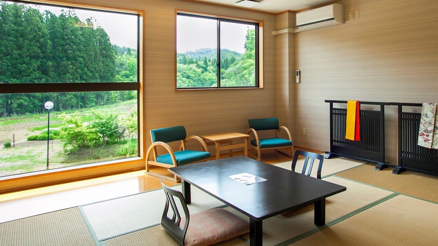 Quarto com piso de tatame, uma mesinha baixa, duas cadeiras, janela com vista para o verde e um painel preto com toalhas.