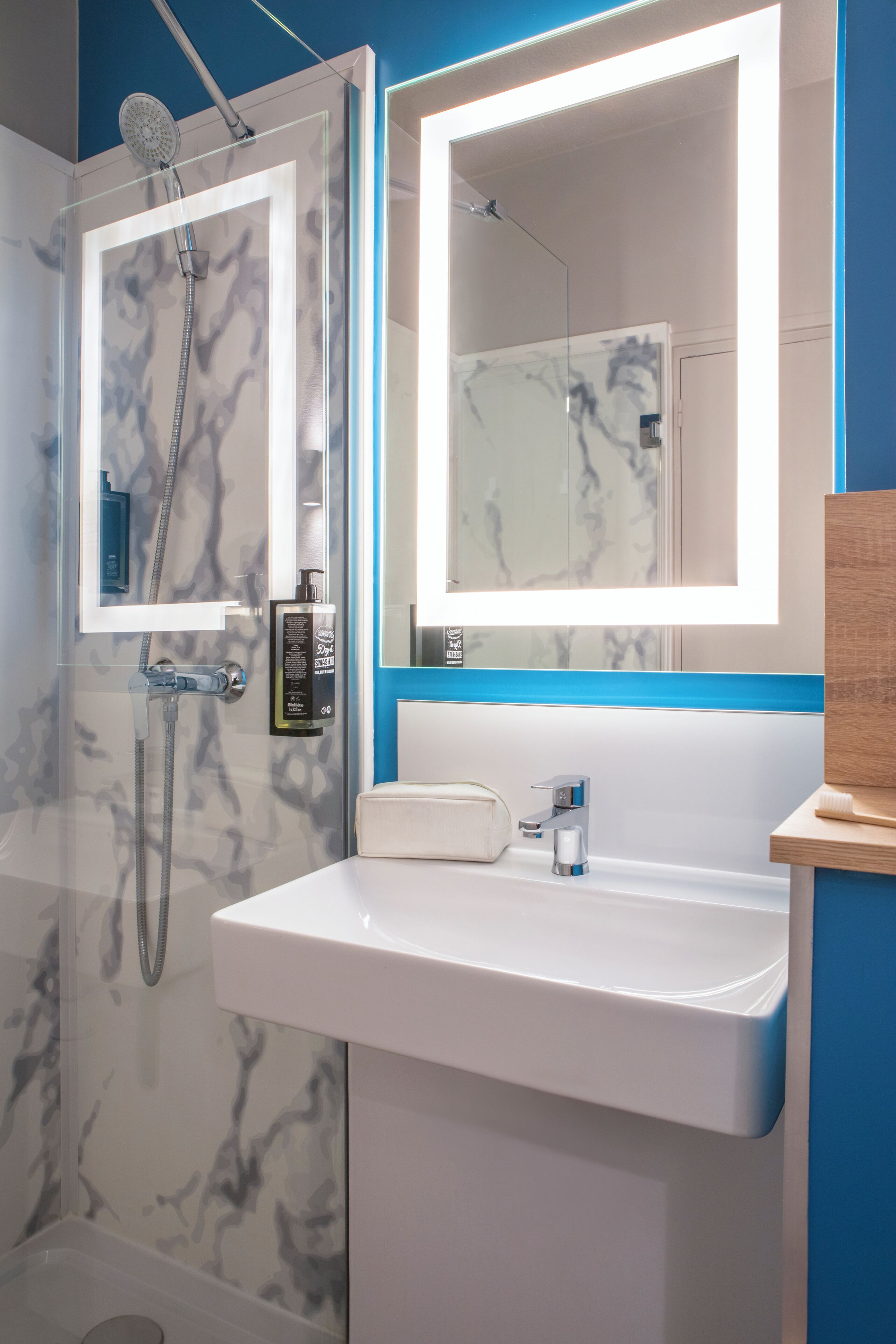 A bathroom with a glass-enclosed shower, a white sink, and a mirror with built-in lighting.