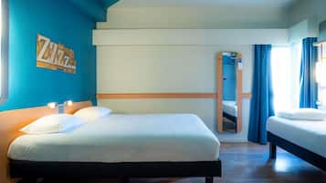 Habitación de hotel con una cama grande, una cama más pequeña, un espejo y una pared azul con un letrero con la letra 'Z'.