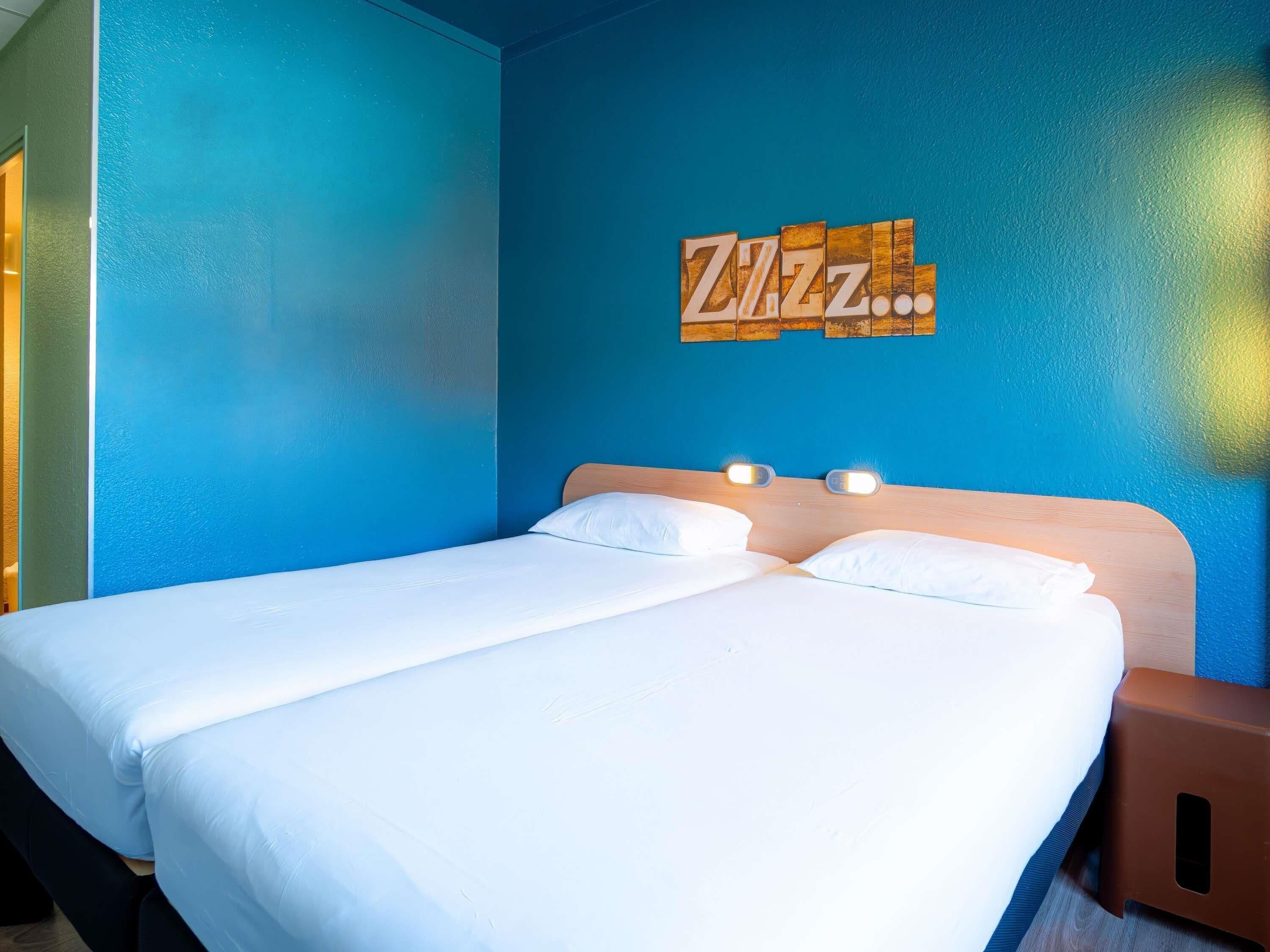 A double bed with white linens, a wooden headboard, and a wall-mounted artwork with the text 'Zzz...'.