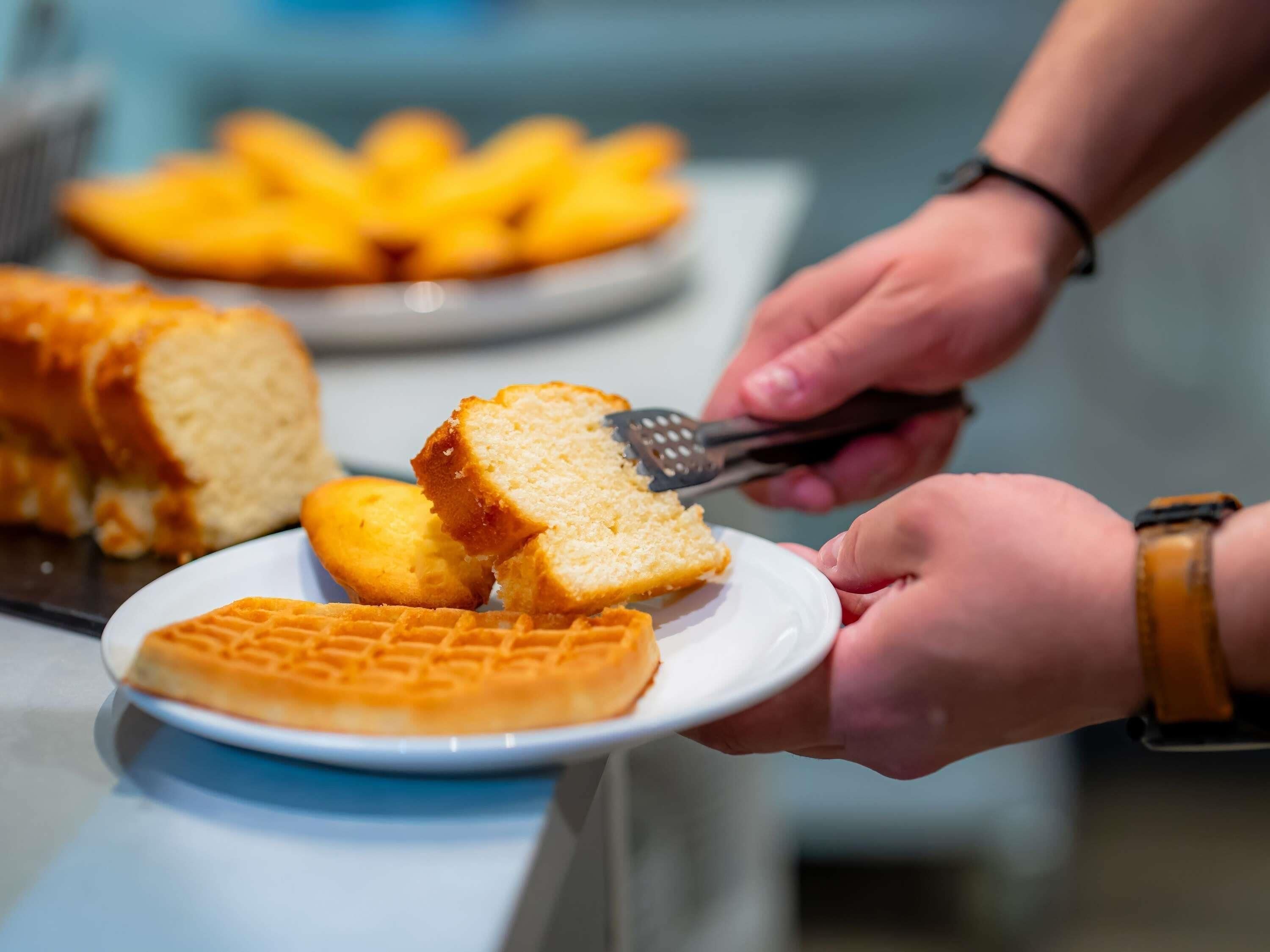 Eine Person serviert Essen, darunter Waffeln und Brot, auf einem Teller.