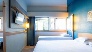 Une chambre d’hôtel avec deux lits, un téléviseur fixé au mur et une fenêtre donnant sur l’extérieur.