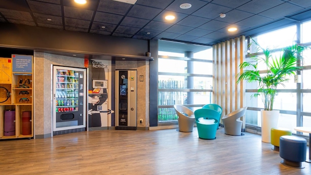 Un hall d’hôtel avec un plancher en bois, des distributeurs automatiques, une enseigne indiquant « Service de qualité » et une grande fenêtre donnant sur un beau paysage.