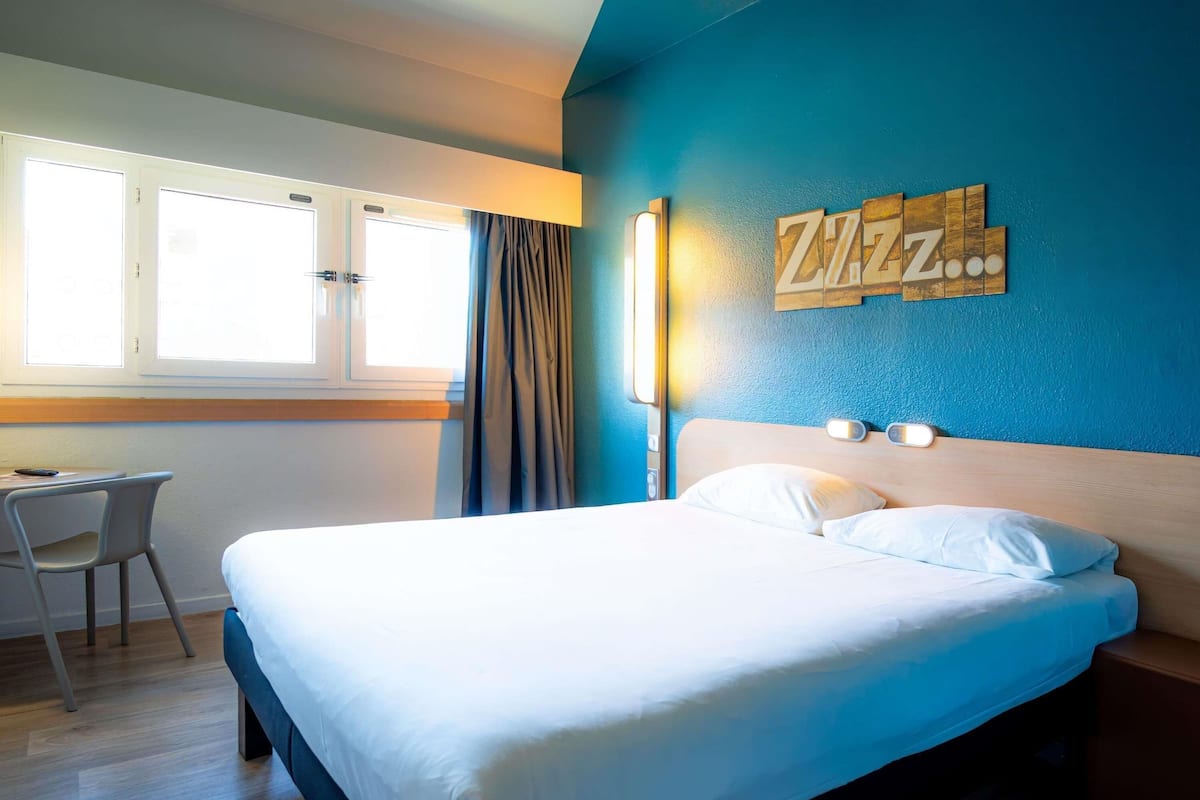 Een hotelkamer met een bed, bureau en raam met gordijnen.
