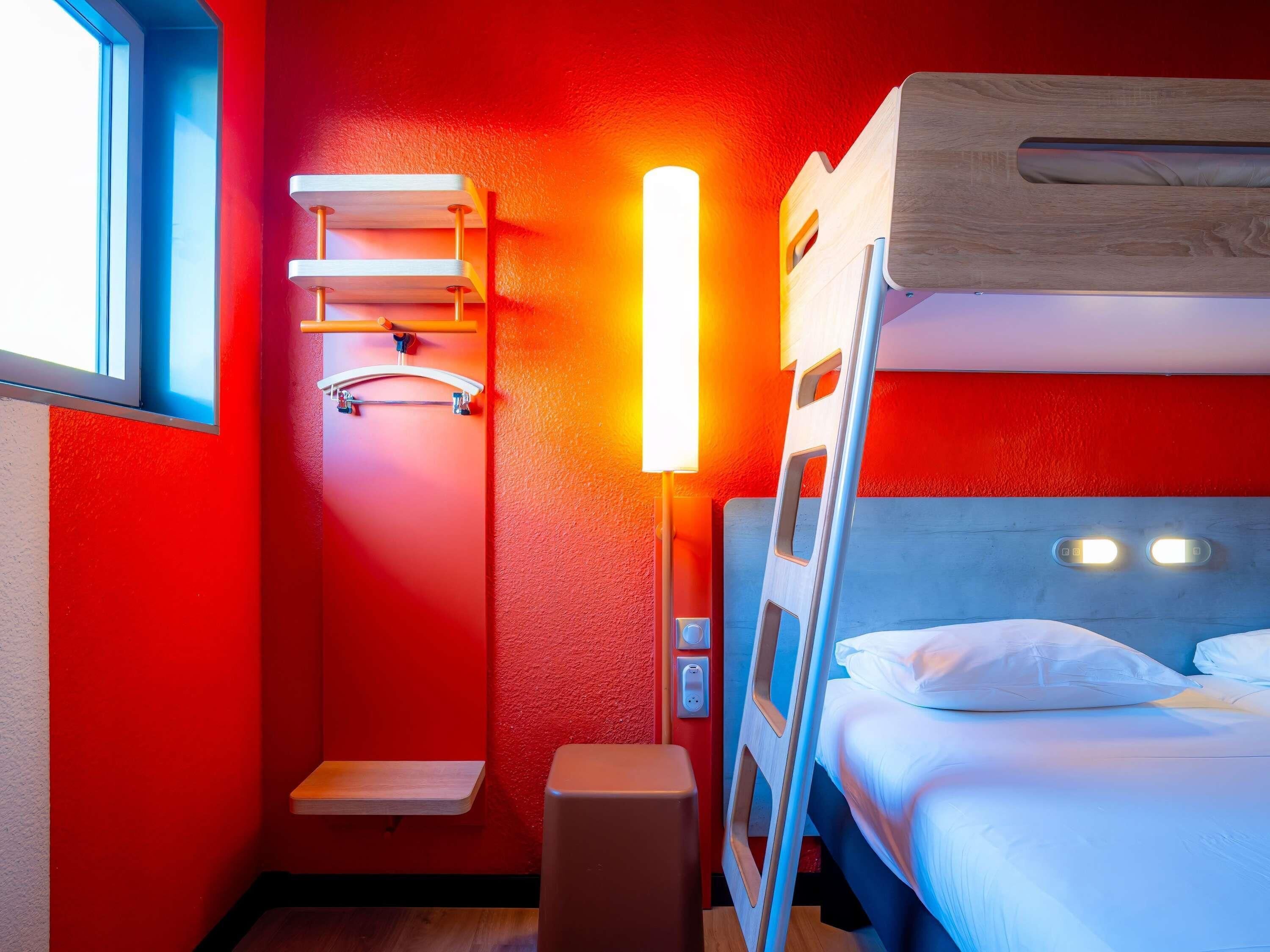 A compact room with a bunk bed, a small shelf, a bench, and a wall-mounted light fixture.
