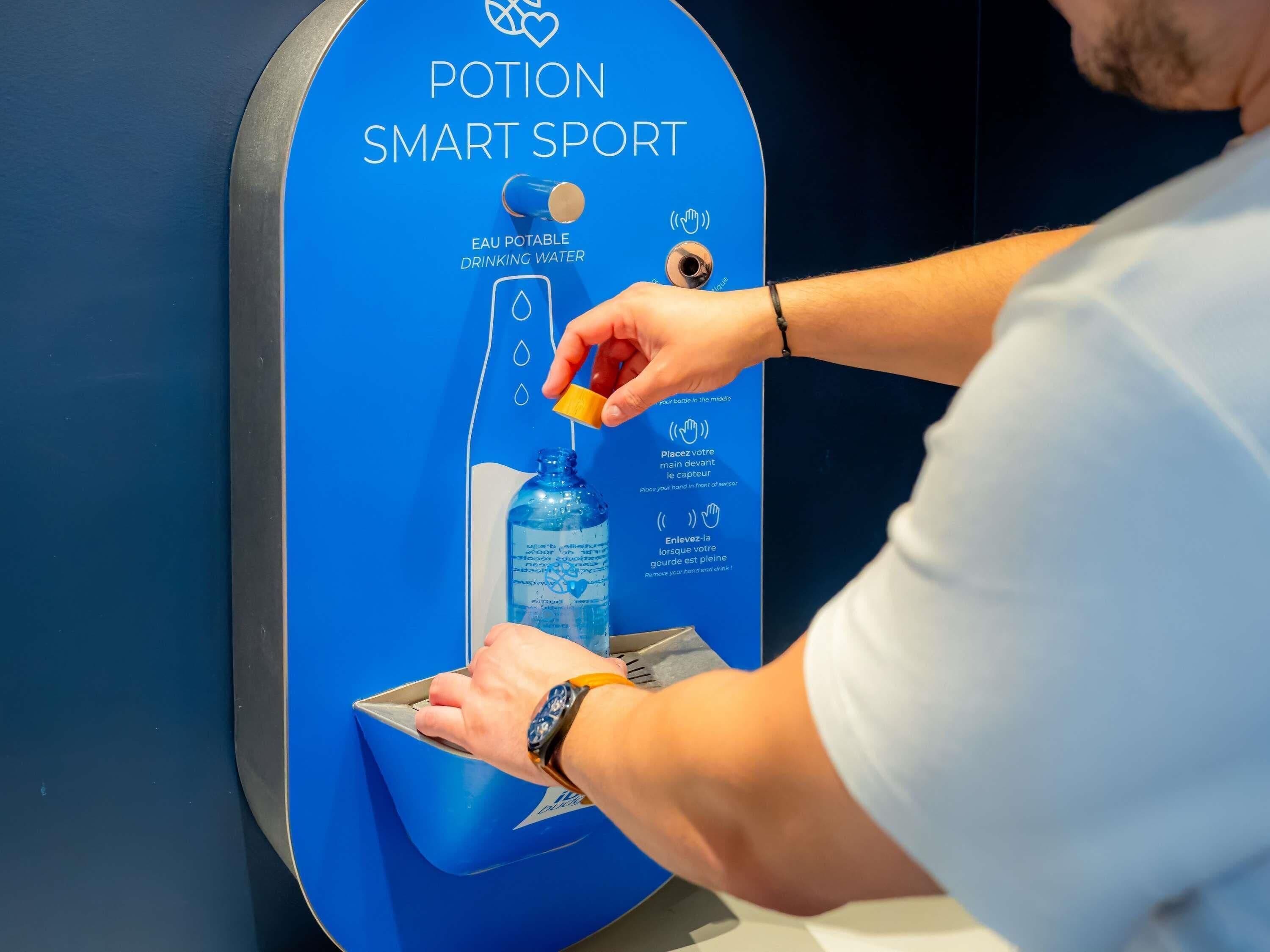 Une personne utilise un distributeur d’eau intelligent dont les instructions sont disponibles dans plusieurs langues.