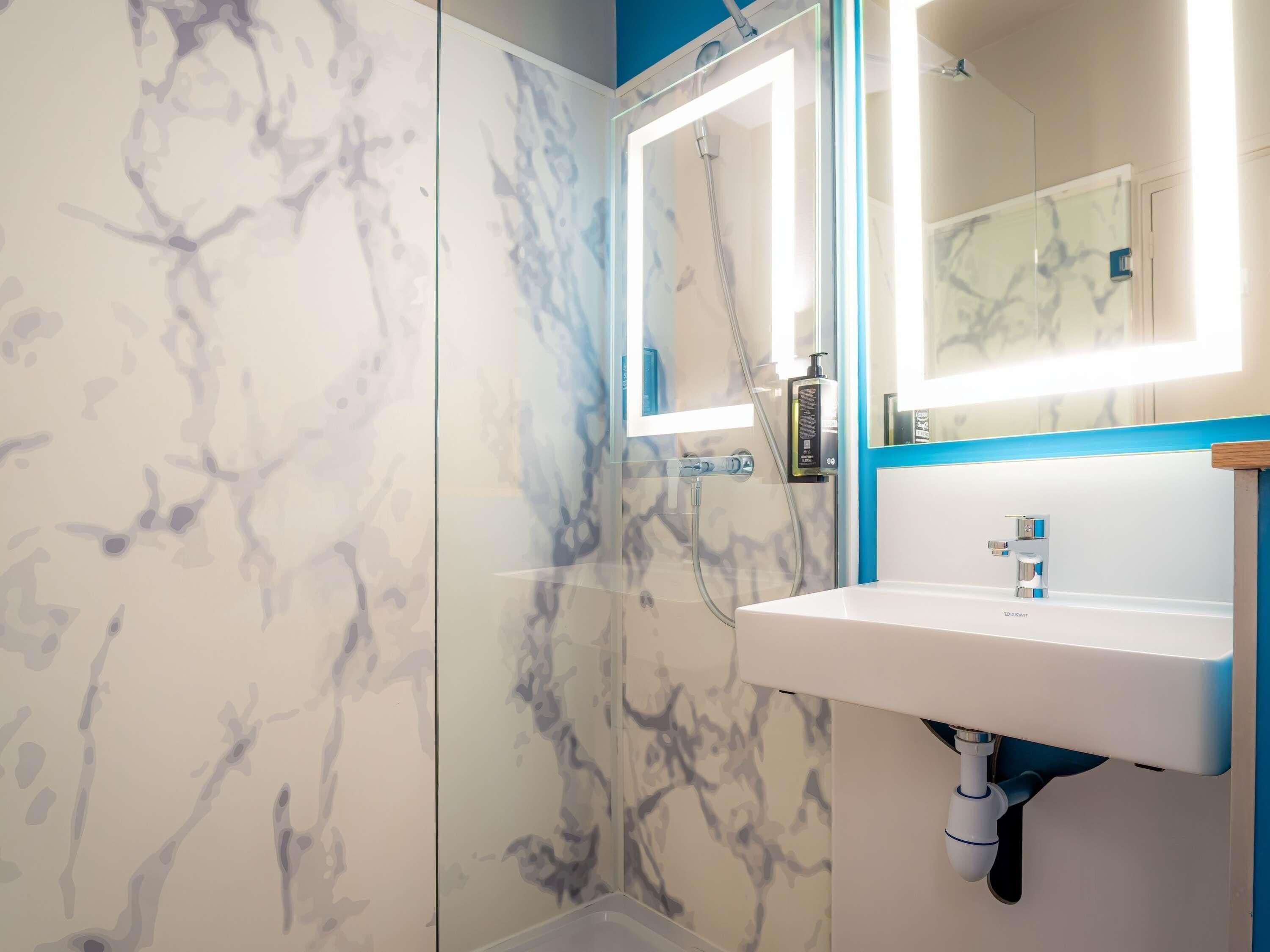 A bathroom with a glass shower enclosure, a white sink, and a mirror with a blue frame.
