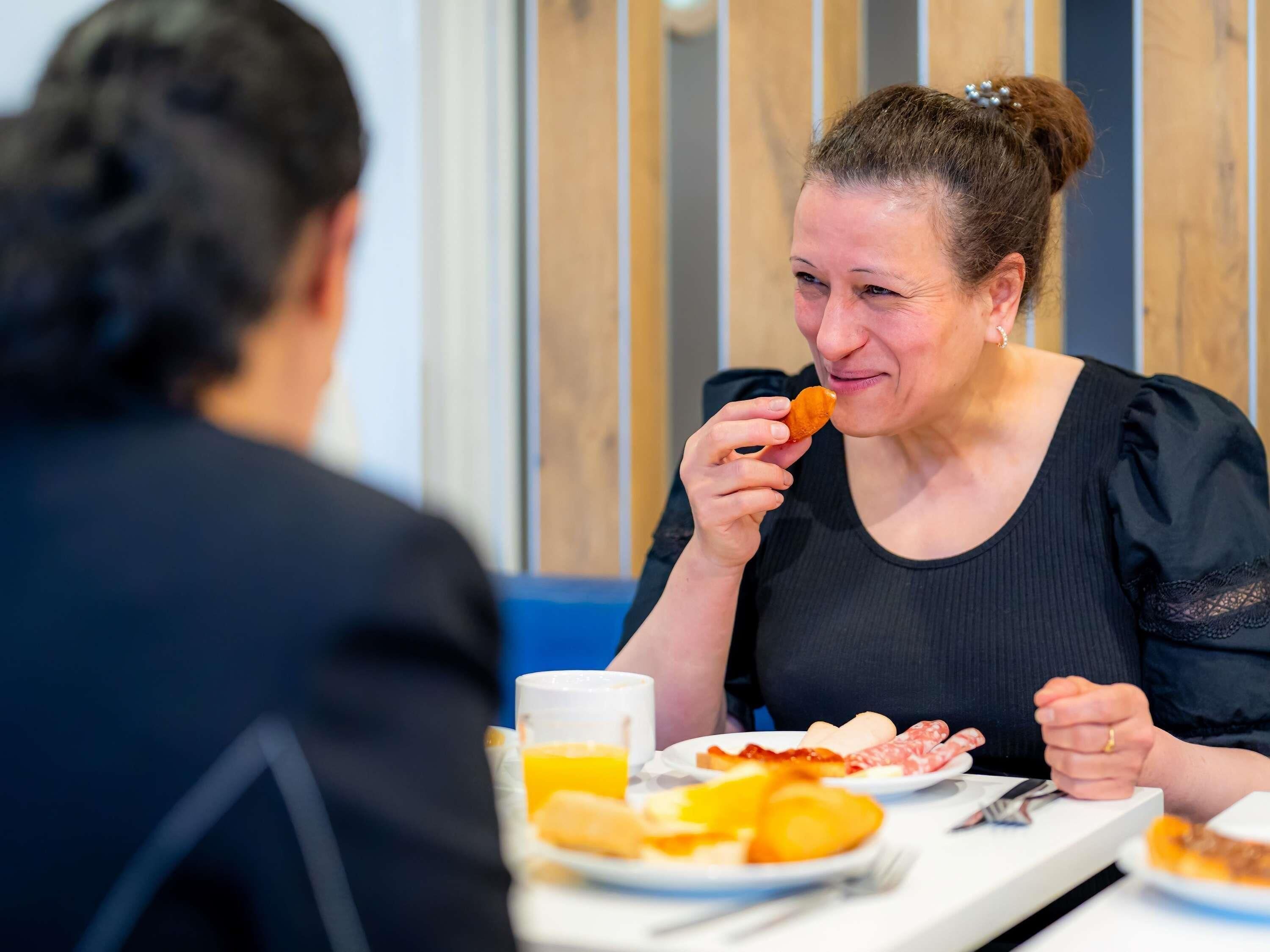 Una persona sentada a una mesa con platos de comida, un vaso de jugo de naranja y una taza.