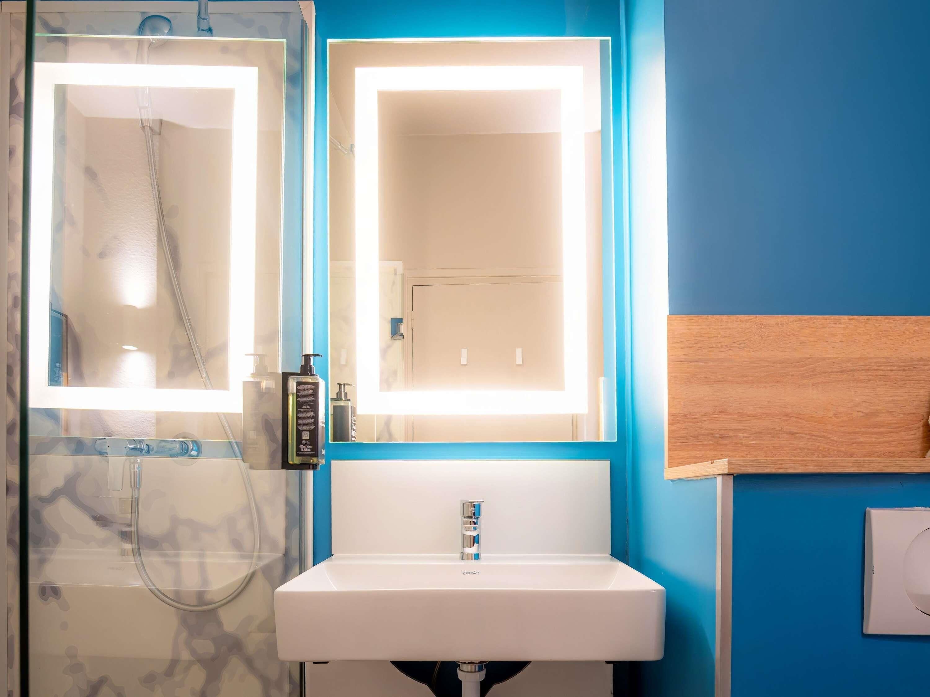 A bathroom with a shower, a sink, and a mirror with built-in lighting.