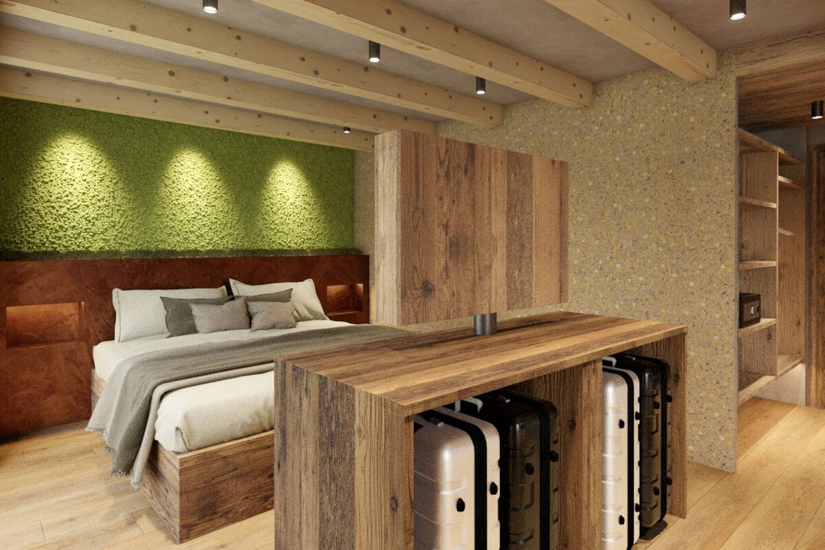 Un dormitorio moderno con cabecera de madera, una cama con varias almohadas, una mesa de madera con maletas debajo y una pared verde con textura.