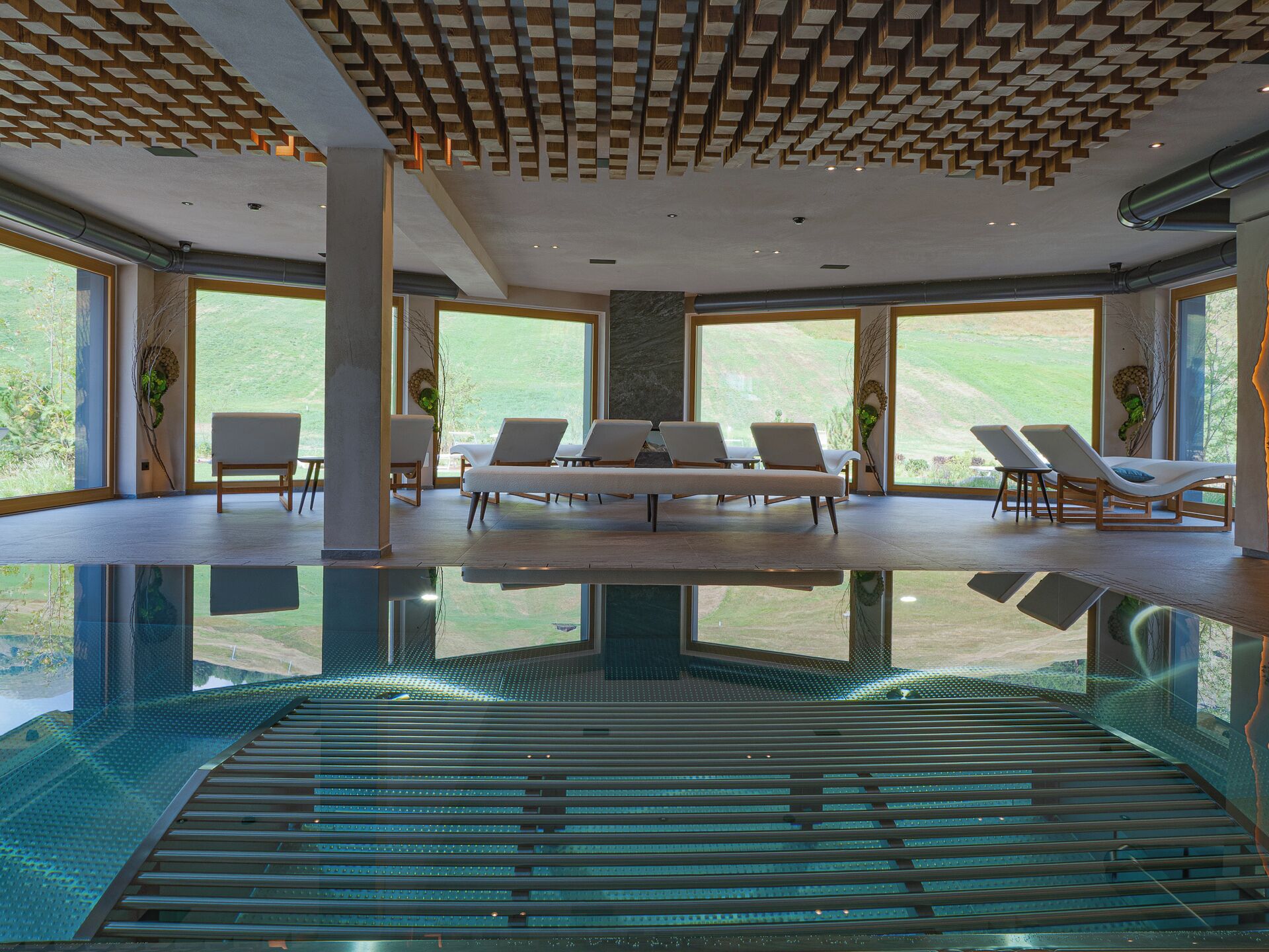 Ein moderner Poolbereich im Innenbereich mit großen Glaswänden, Liegestühlen und einem außergewöhnlichen Deckenstil.