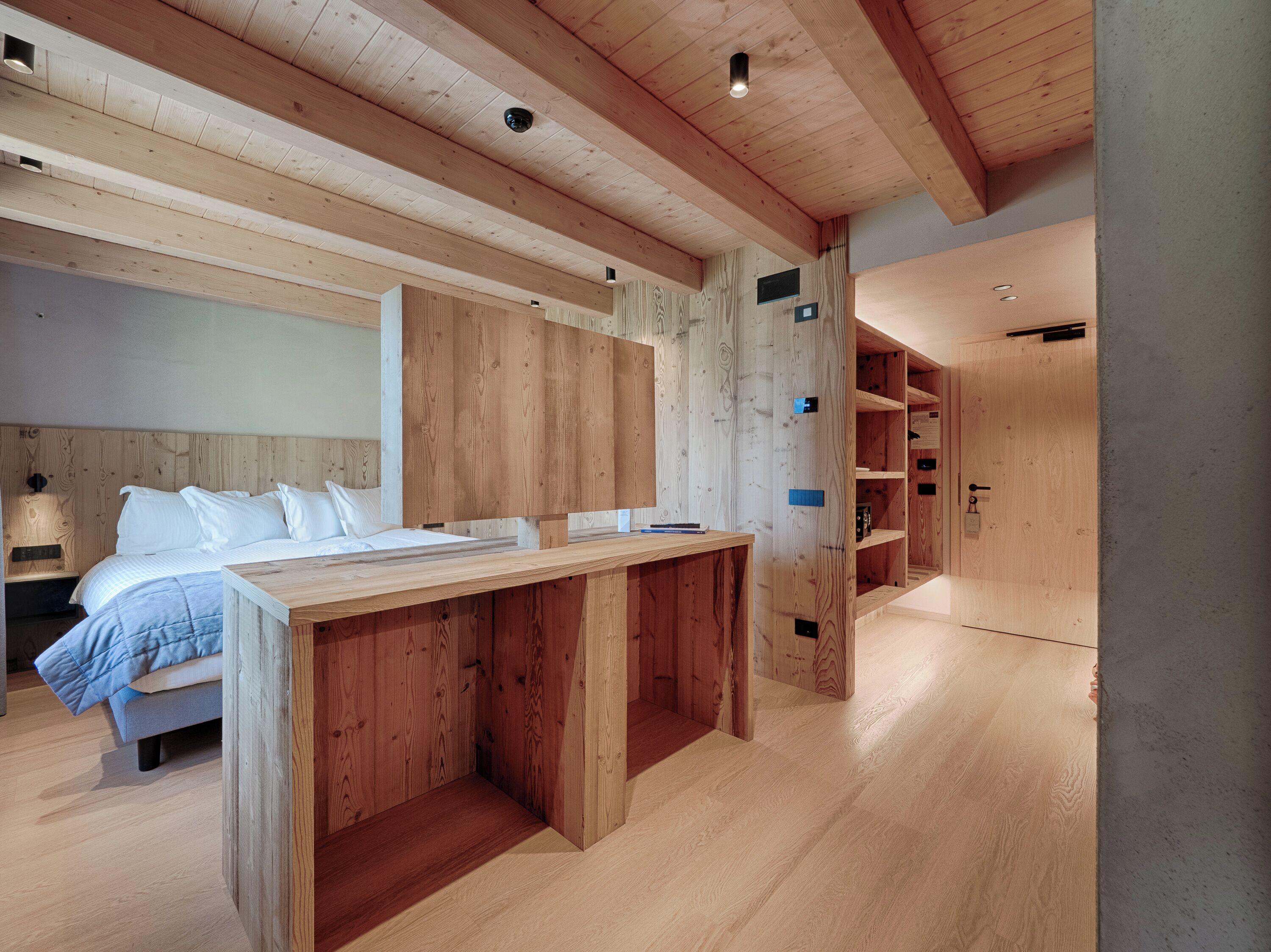 Una habitación moderna con techo de madera, una cama con ropa de cama blanca, un escritorio de madera y estanterías empotradas.