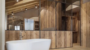 Ein modernes Badezimmer mit einer freistehenden Badewanne, Holzwandverkleidung und einem großen Spiegel, der den Raum widerspiegelt.