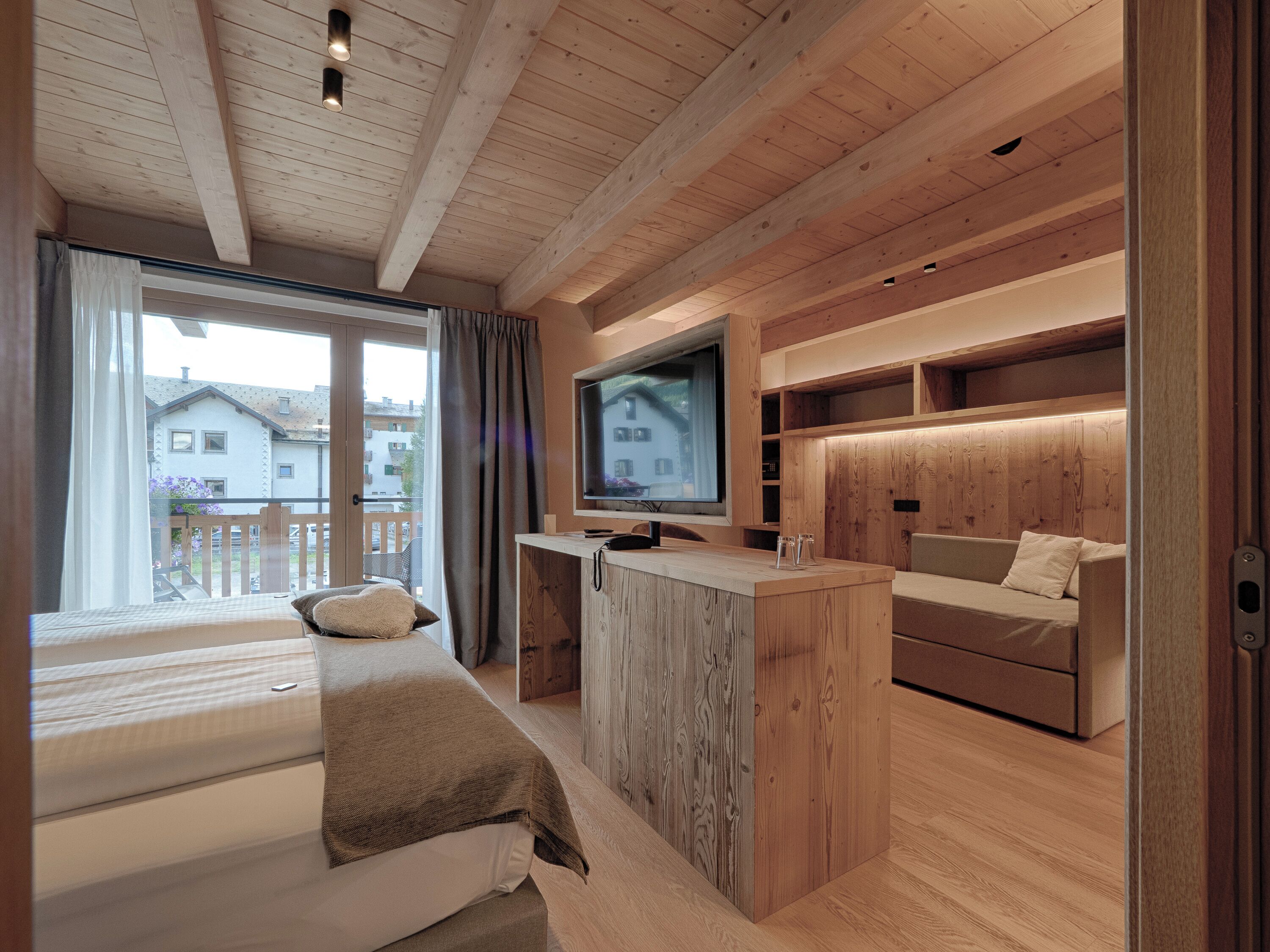 Quarto moderno com cama, escrivaninha de madeira, televisão e sofá.
