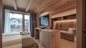 Quarto moderno com cama, escrivaninha de madeira, televisão e sofá.