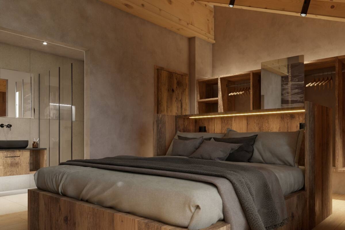 Un dormitorio moderno con cabecera de madera, una cama grande con muchas almohadas, una mesita de noche y un banco empotrado al pie de la cama.