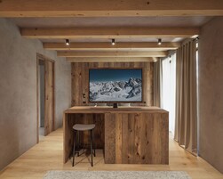 Un interno moderno con un’area bar in legno, un grande televisore montato a parete e vista sulle montagne innevate.