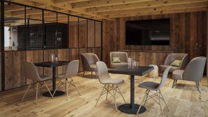 A modern interior with wooden beams, a dining area with tables and chairs, a kitchen with a wine rack, and a flat-screen TV mounted on the wall. - Al Nin Hotel&Spa (Livigno)