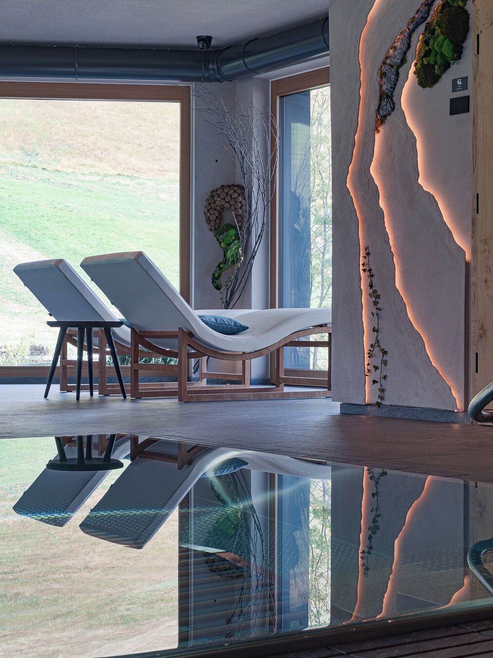 A modern interior with a glass pool, lounge chairs, and a view of the outdoors.