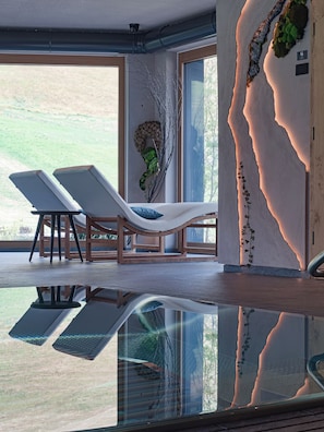 A modern interior with a glass pool, lounge chairs, and a view of the outdoors. - Al Nin Hotel&Spa (Livigno)