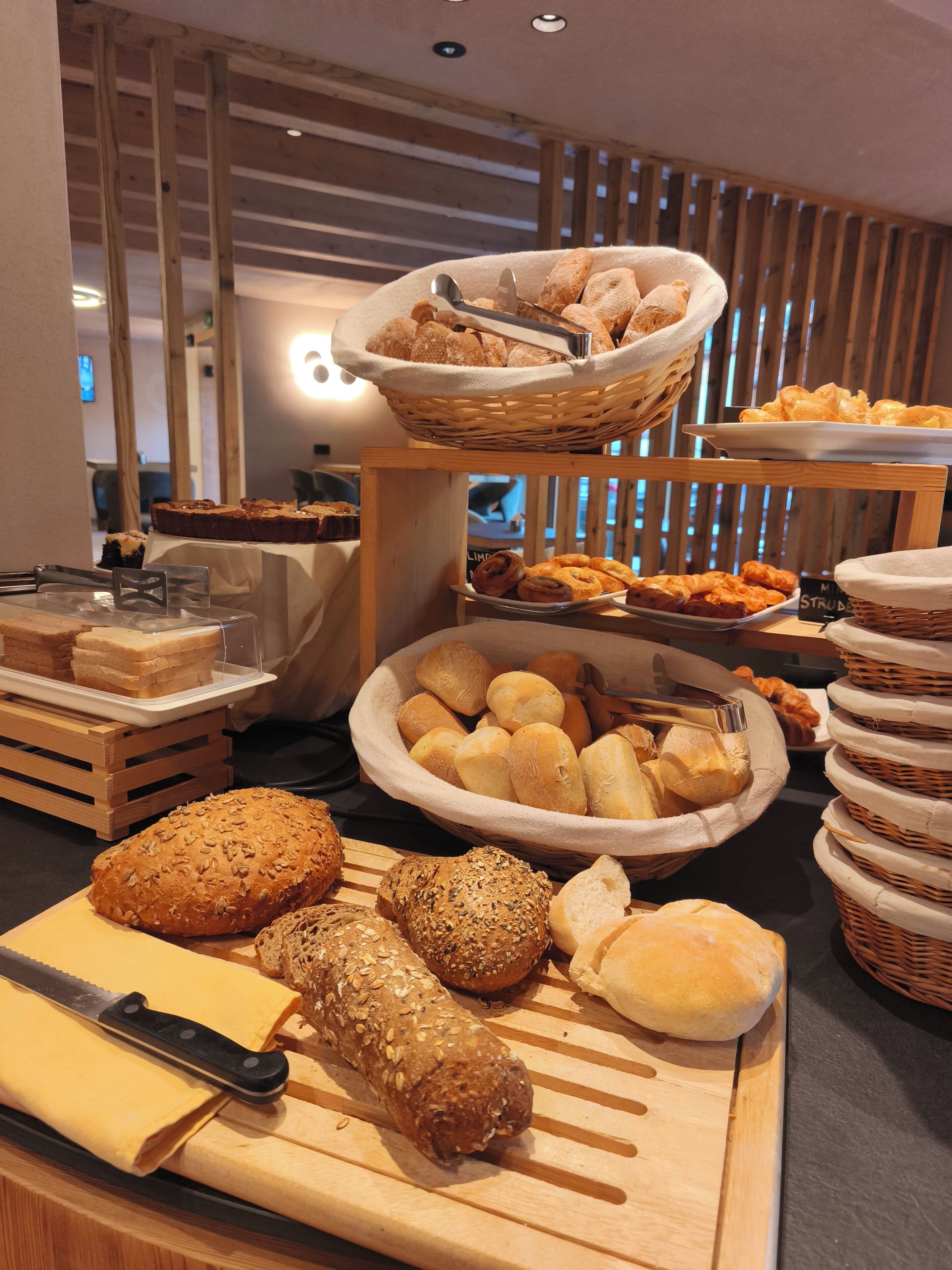 Un buffet proposant une variété de pains et de viennoiseries, notamment un grand saladier rempli de petits pains et un plateau de tranches de pain.