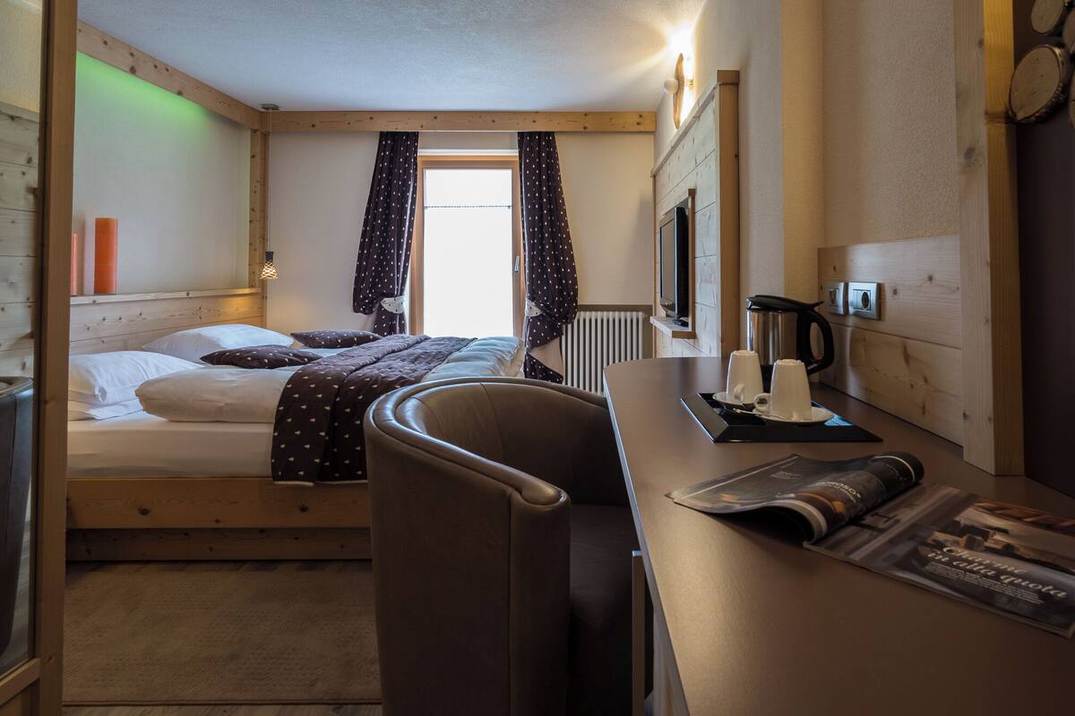 Habitación de hotel compacta con cama, escritorio con hervidor y una silla.