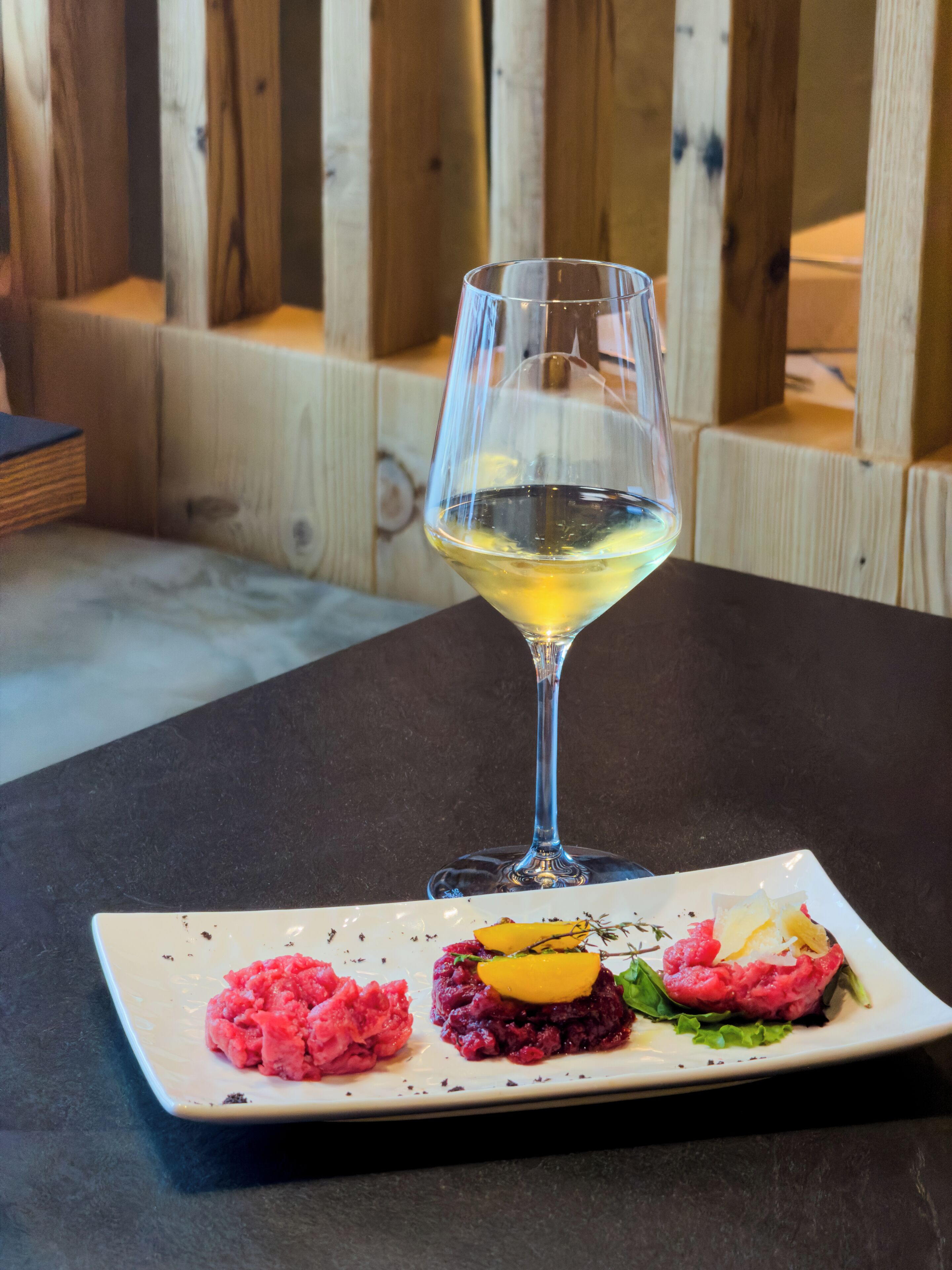 A glass of white wine on a table with a plate of food.