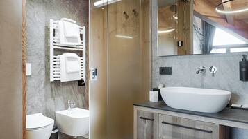 Un baño moderno con un lavamanos grande blanco, un bidé y un inodoro. Hay un mueble de tocador de madera con un espejo sobre el lavamanos.