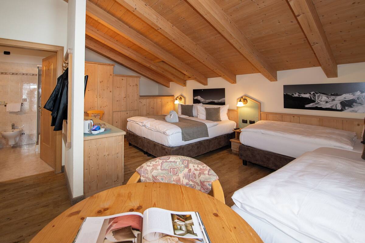 Un dormitorio acogedor en el ático con vigas de madera, dos camas, un escritorio pequeño y un baño.