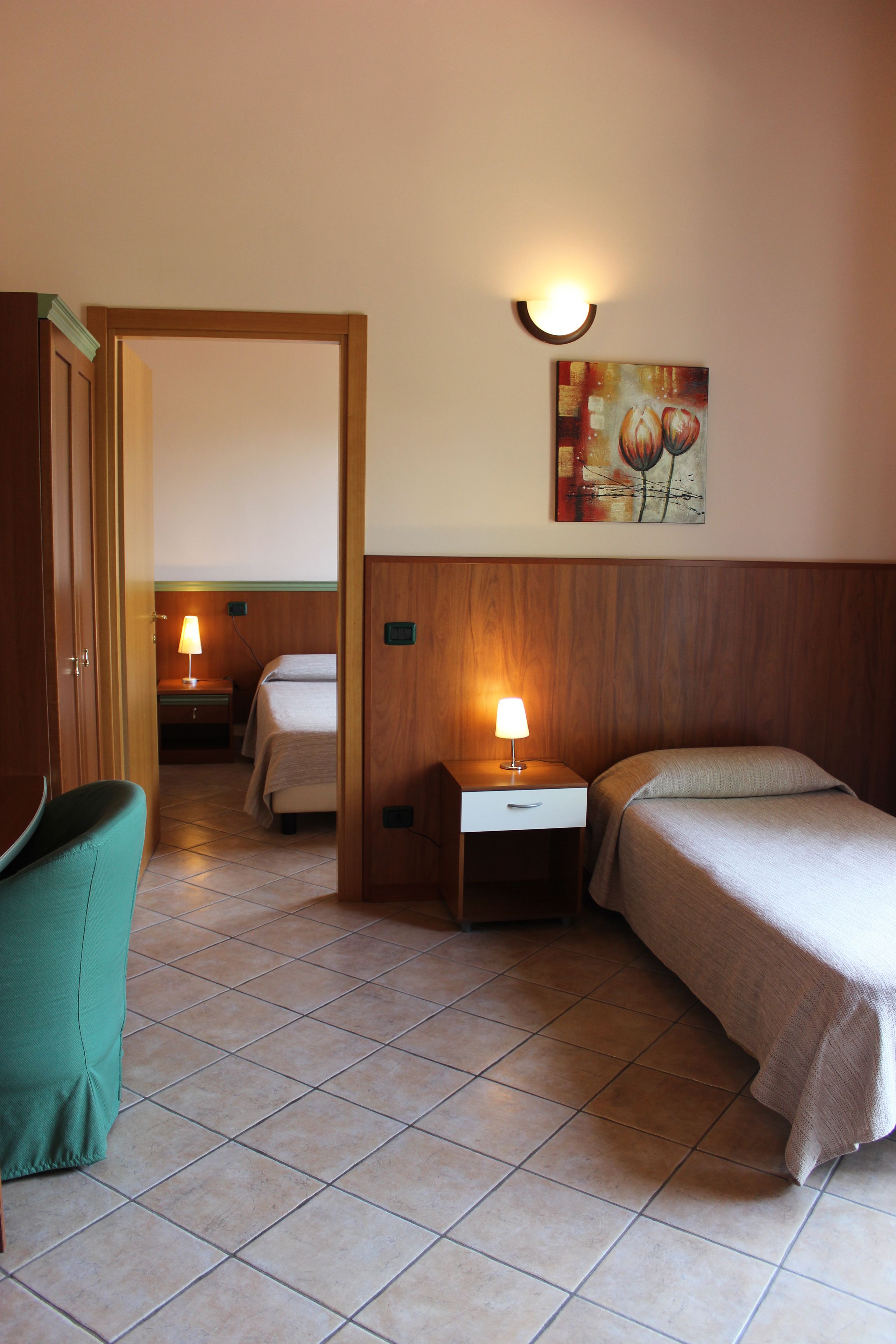 A hotel room with a bed, a chair, a nightstand with a lamp, and a painting on the wall.