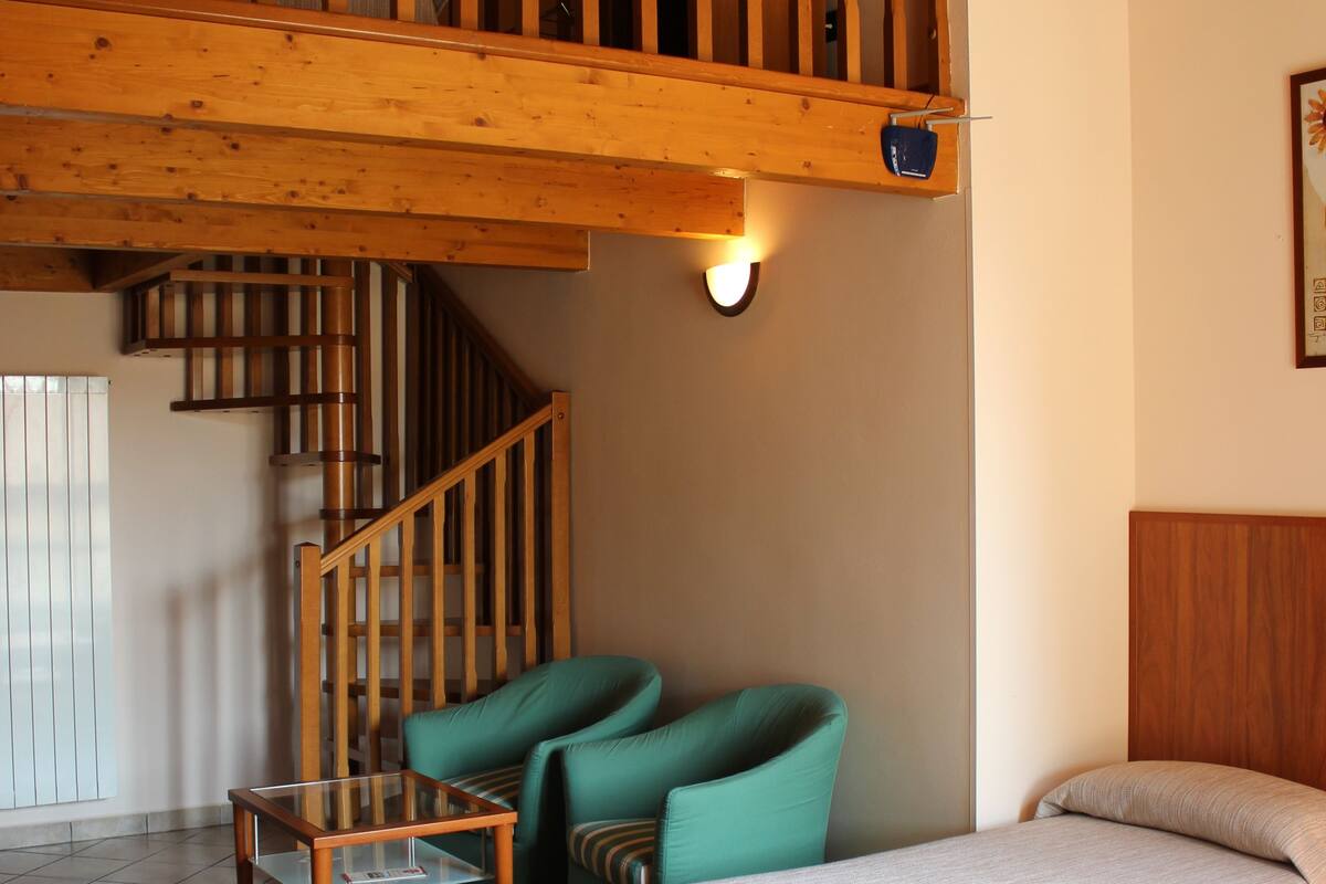 Une pièce avec un escalier en bois, deux lits, une chaise et une petite table.