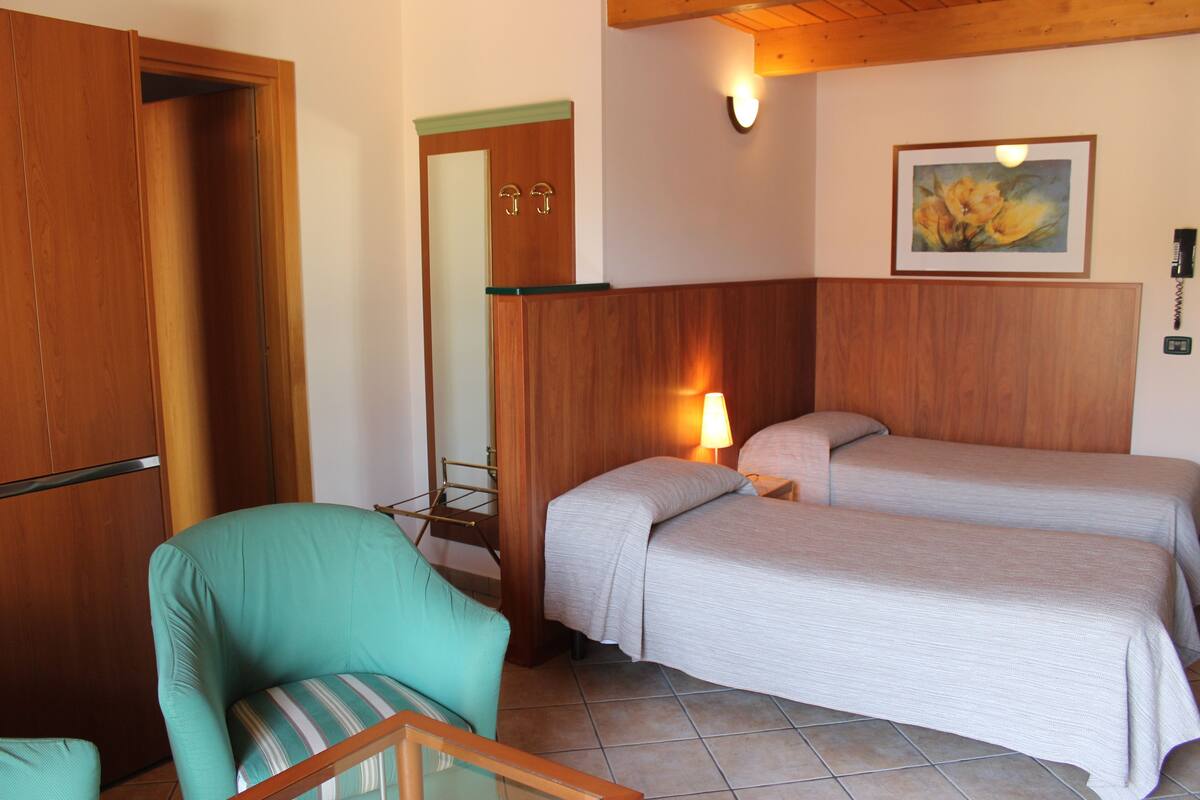 Une chambre avec deux lits, une armoire en bois, une chaise et un tableau accroché au mur.