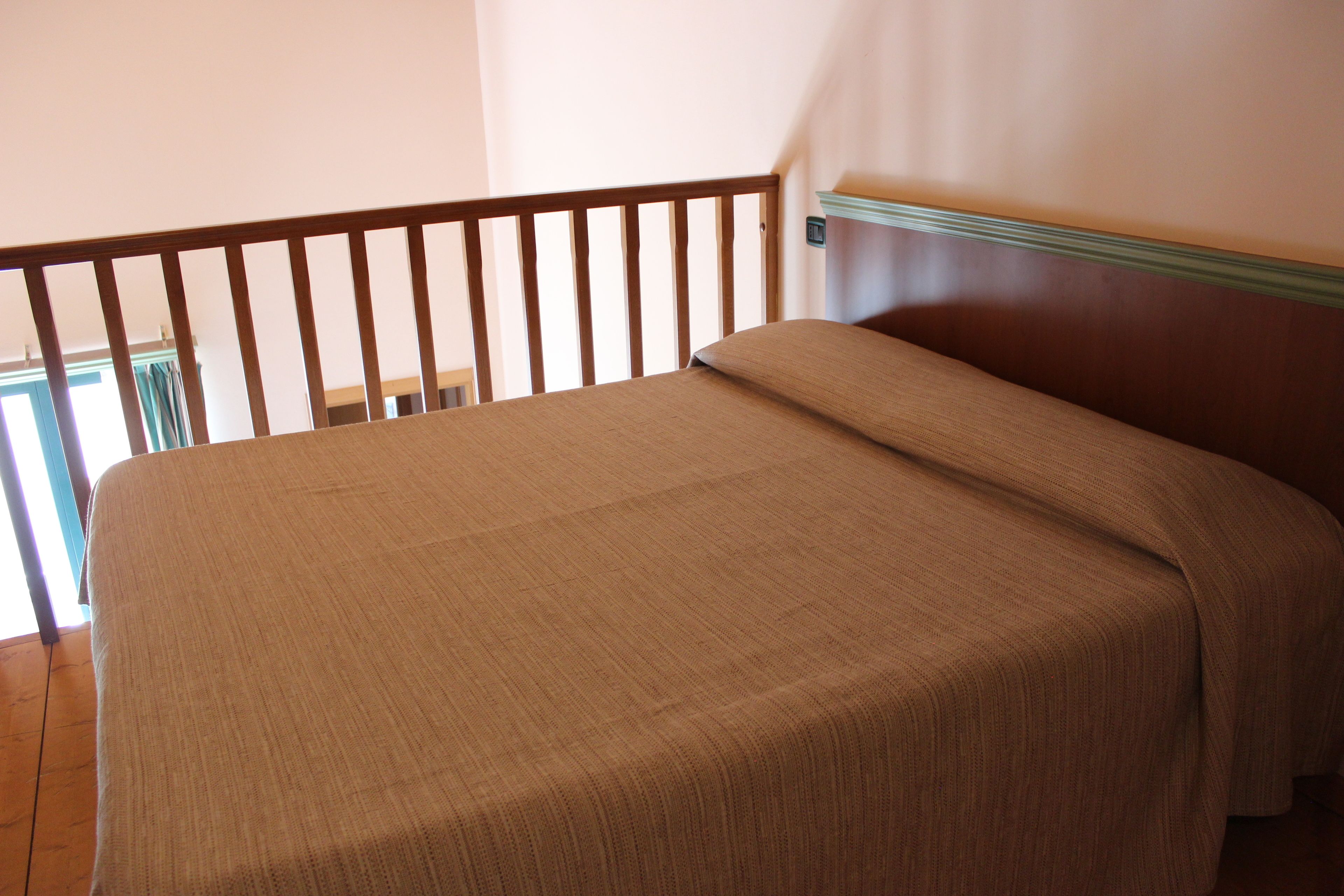 Un dormitorio con cabecera de madera, cama con cubrecama color beige y vista a un balcón.