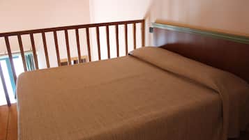 Un dormitorio con cabecera de madera, cama con cubrecama color beige y vista a un balcón.