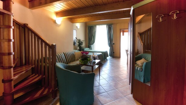 A spacious living area with a wooden staircase, a sofa, a coffee table, and a view of a bedroom through an open door. - B&B Villa Giglio (Arsago Seprio)