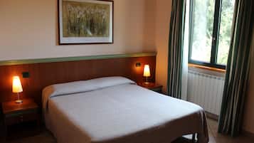 A hotel room with a bed, two bedside lamps, a framed artwork on the wall, a window with curtains, and a radiator.
