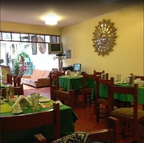 A restaurant with multiple tables and chairs, a television mounted on the wall, and a decorative wall piece. - Hotel Casablanca (Cusco)