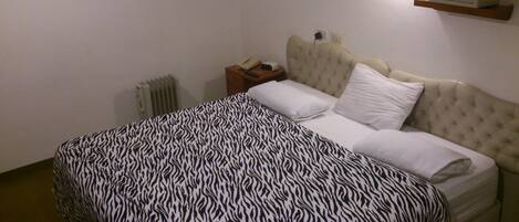 A bedroom with a zebra-patterned bedspread, a tufted headboard, a bedside table with a telephone, and a wall-mounted TV.