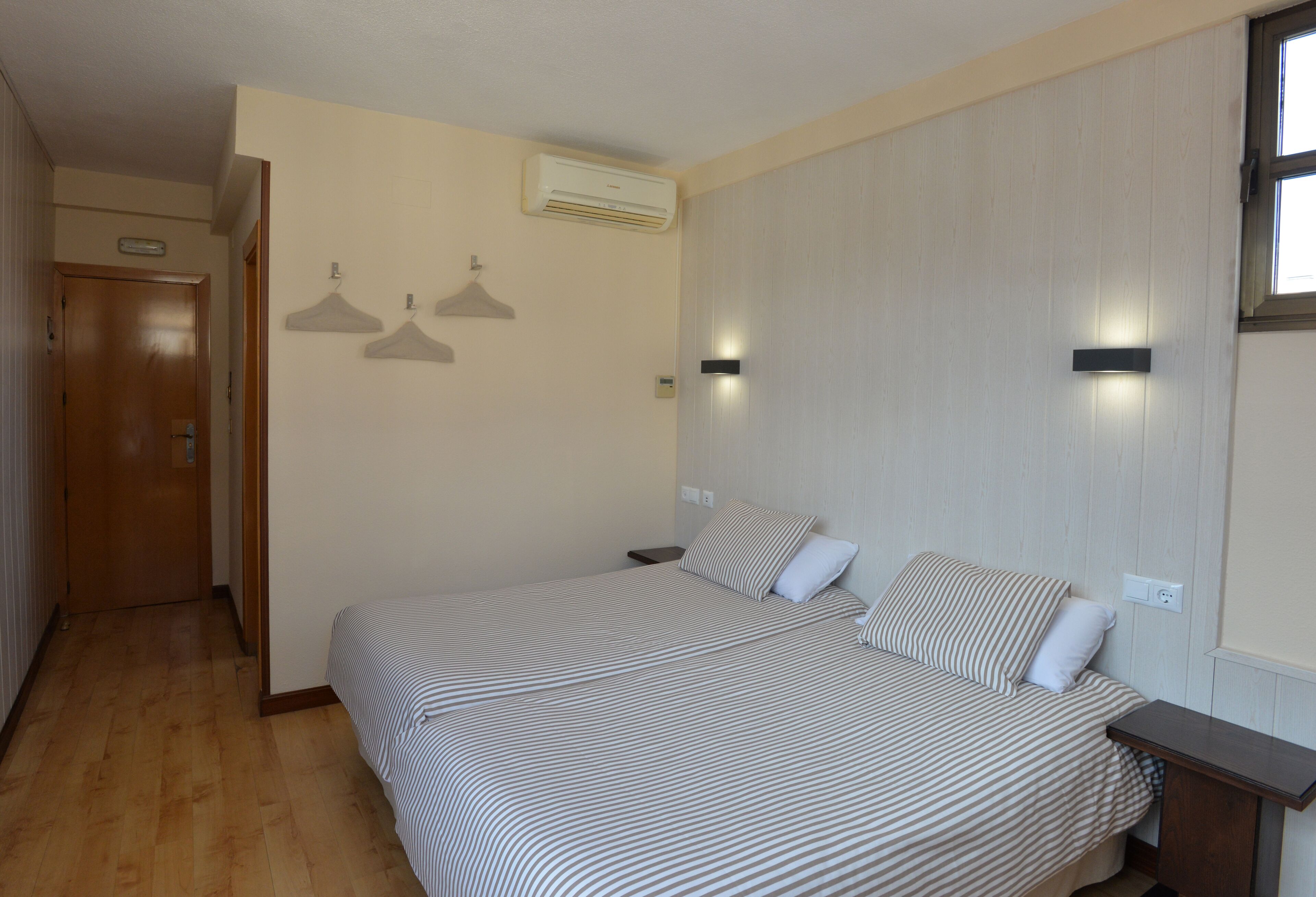 Une chambre à coucher avec un grand lit, deux tables de chevet, un plancher en bois, une porte et une fenêtre.