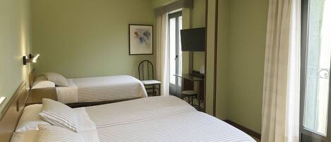 A hotel room with two beds, a desk, a chair, a TV, and a window with curtains.