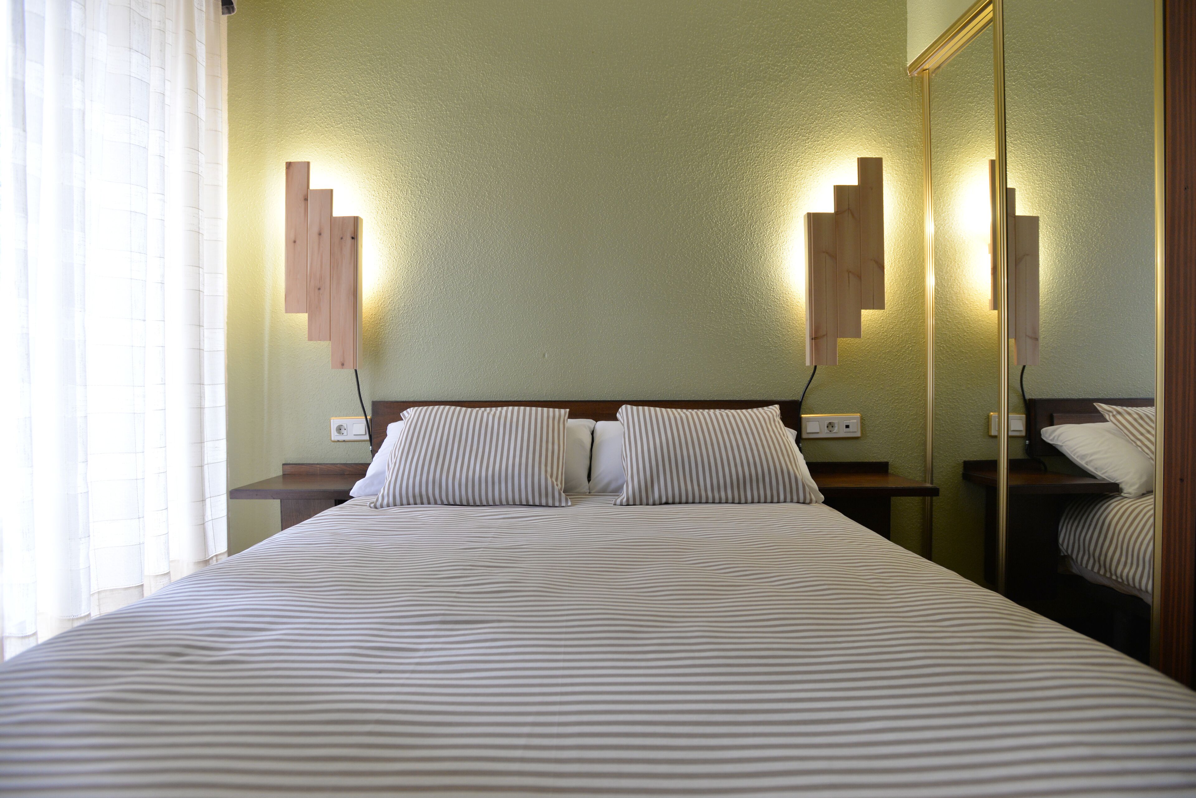 A hotel room with a large bed, two bedside tables, a mirror, and a wall-mounted light fixture.